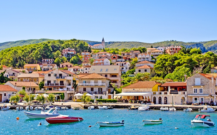 Boats docked at the Port of Jelsa, Hvar island, Croatia, with hillside houses in the background.