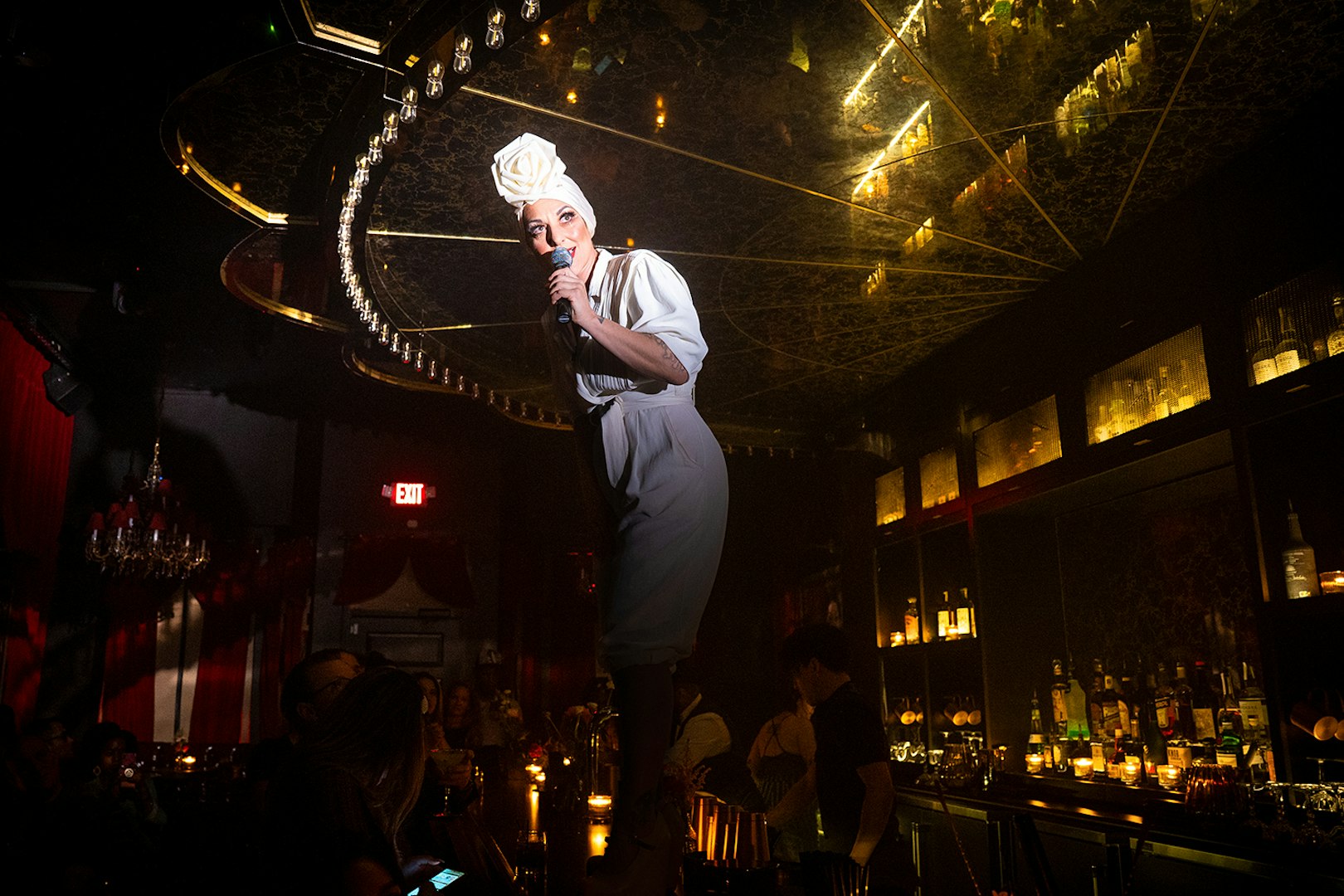 Performer on bar counter during Miss Behaves: Maverick's Variety Show in dimly lit venue.