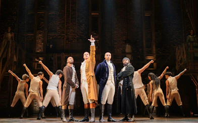 Cast performing Hamilton on West End stage, actors in period costumes.