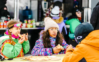 Children enjoying pizza at Farellones Park, Santiago, during a snowy day trip.