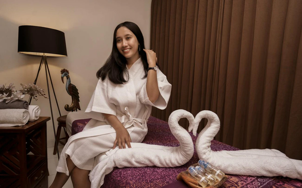 Woman in a spa robe sitting on a massage table with towel swans, Dubai.