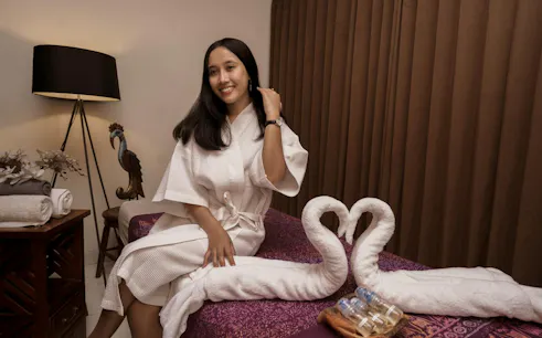 Woman in a spa robe sitting on a massage table with towel swans, Dubai.