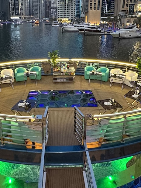 Lotus Mega Yacht deck with seating and tables, Dubai Marina in the background.