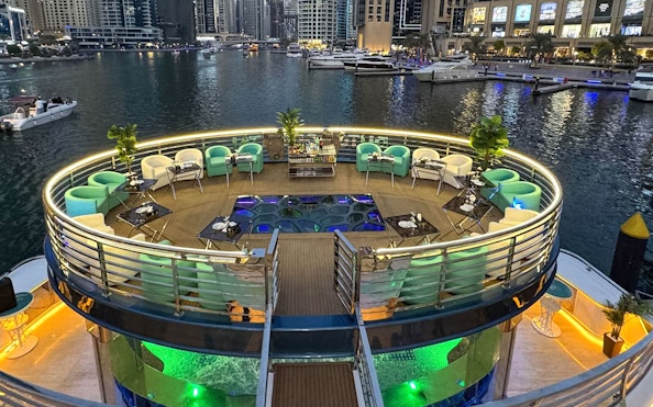 Lotus Mega Yacht deck with seating and tables, Dubai Marina in the background.