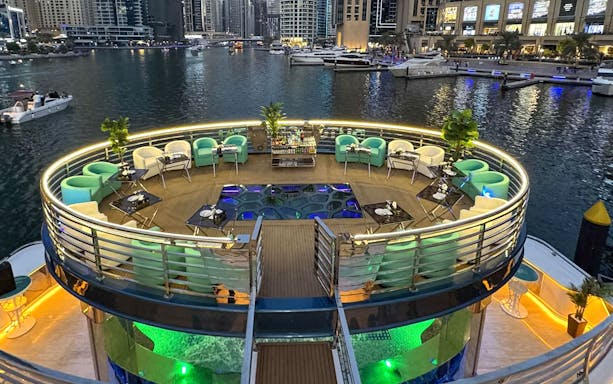Lotus Mega Yacht deck with seating and tables, Dubai Marina in the background.