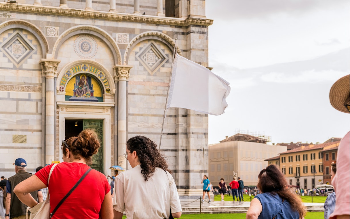 Tour group outside Pisa Cathedral with guide holding a white flag.