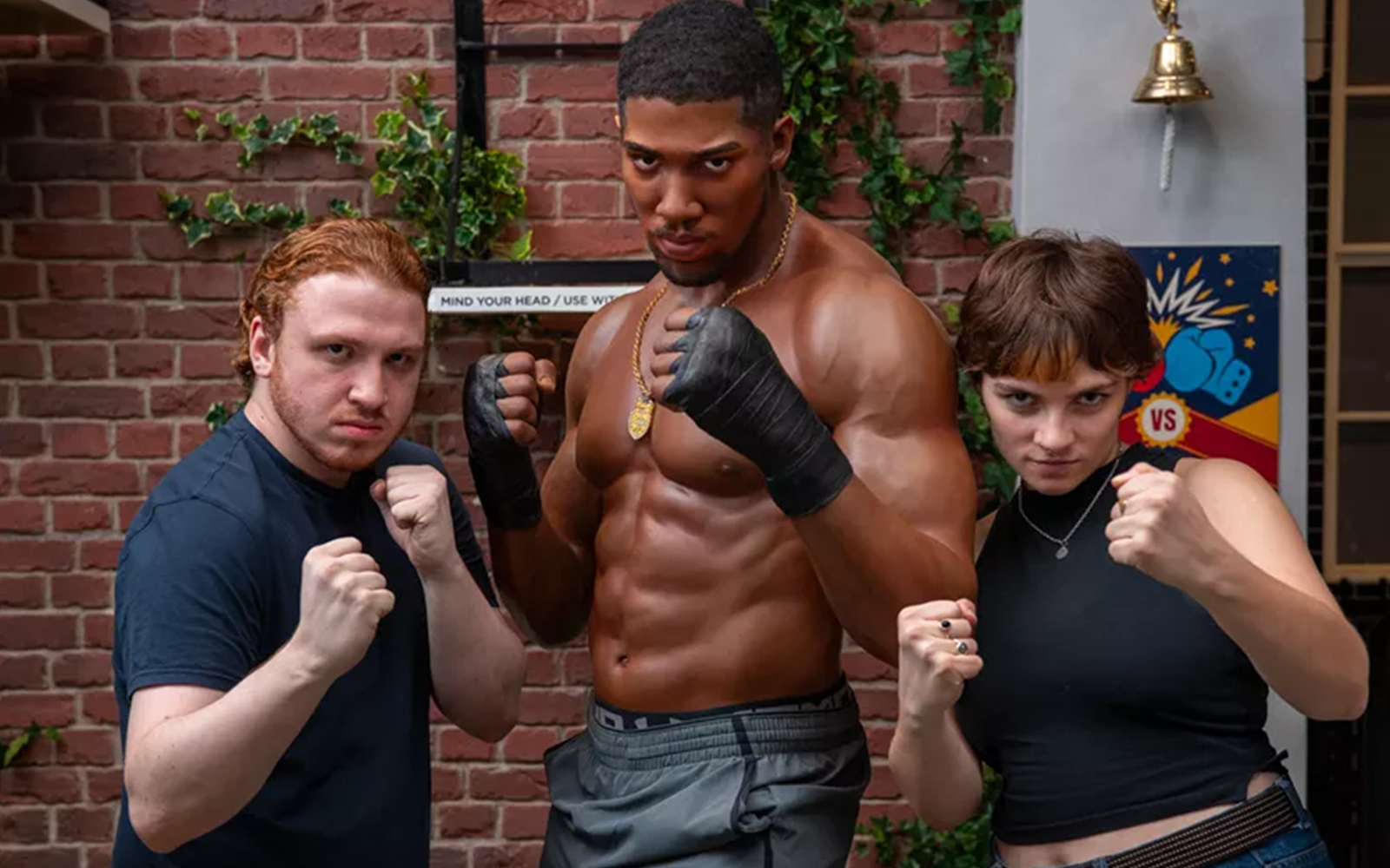 Boxer Anthony Joshua wax figure, and two tourists posing besides him with their fists clenched