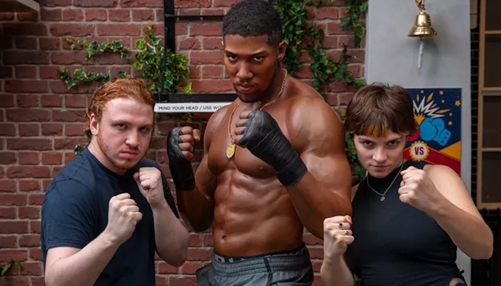 Boxer Anthony Joshua wax figure, and two tourists posing besides him with their fists clenched