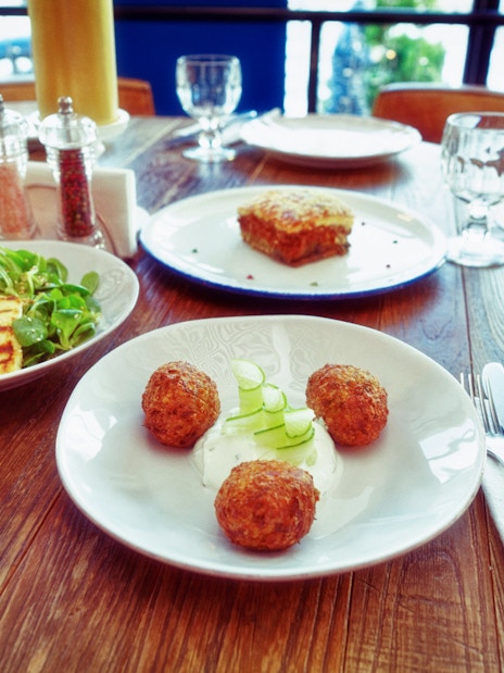 Three Greek dishes on a table: fried Saganaki cheese, moussaka, and zucchini fritters.