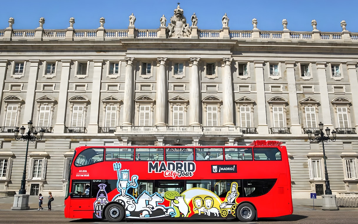 Red Madrid City Tour bus in front of the Royal Palace, part of Museum of Illusions and bus tour combo.