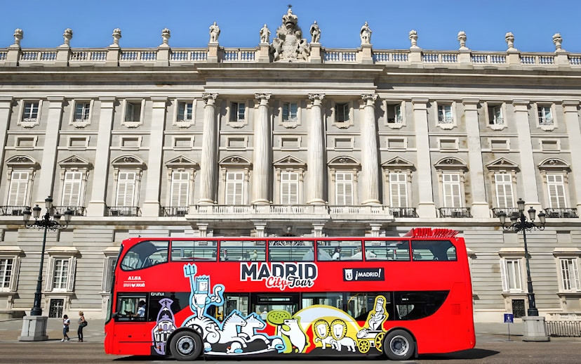 Red Madrid City Tour bus in front of the Royal Palace, part of Museum of Illusions and bus tour combo.