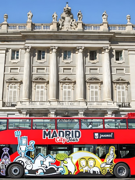 Red Madrid City Tour bus in front of the Royal Palace, part of Museum of Illusions and bus tour combo.