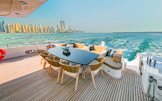 Super-yacht deck with dining table, Dubai Marina skyline in background.