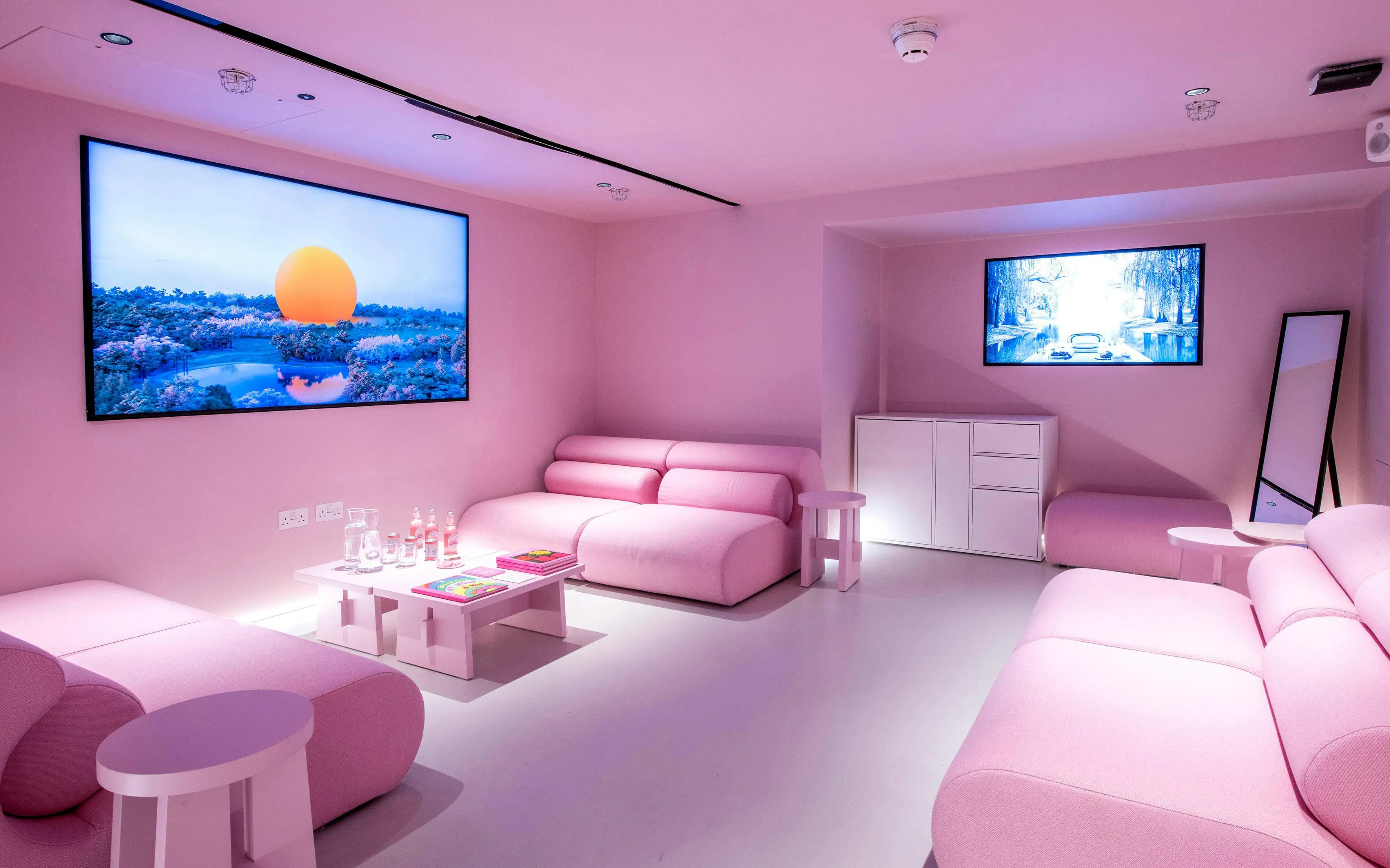Pink-themed room with modern sofas and digital art displays at Moco Museum, London.