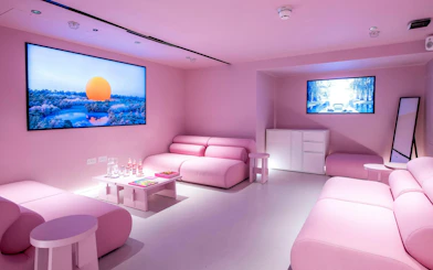Pink-themed room with modern sofas and digital art displays at Moco Museum, London.
