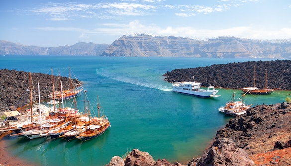 Boats docked near volcanic rocks at Nea Kameni, Santorini, with caldera view.