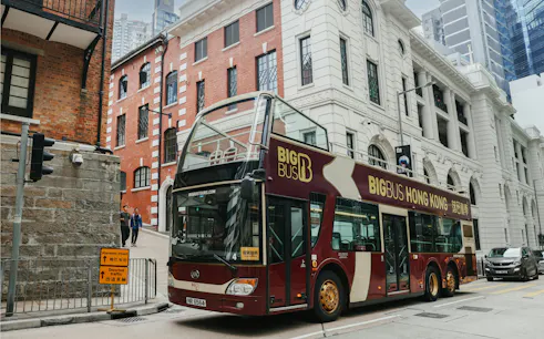 Hop-on hop-off bus in Hong Kong near historic buildings, part of Victoria Harbor ferry tour.