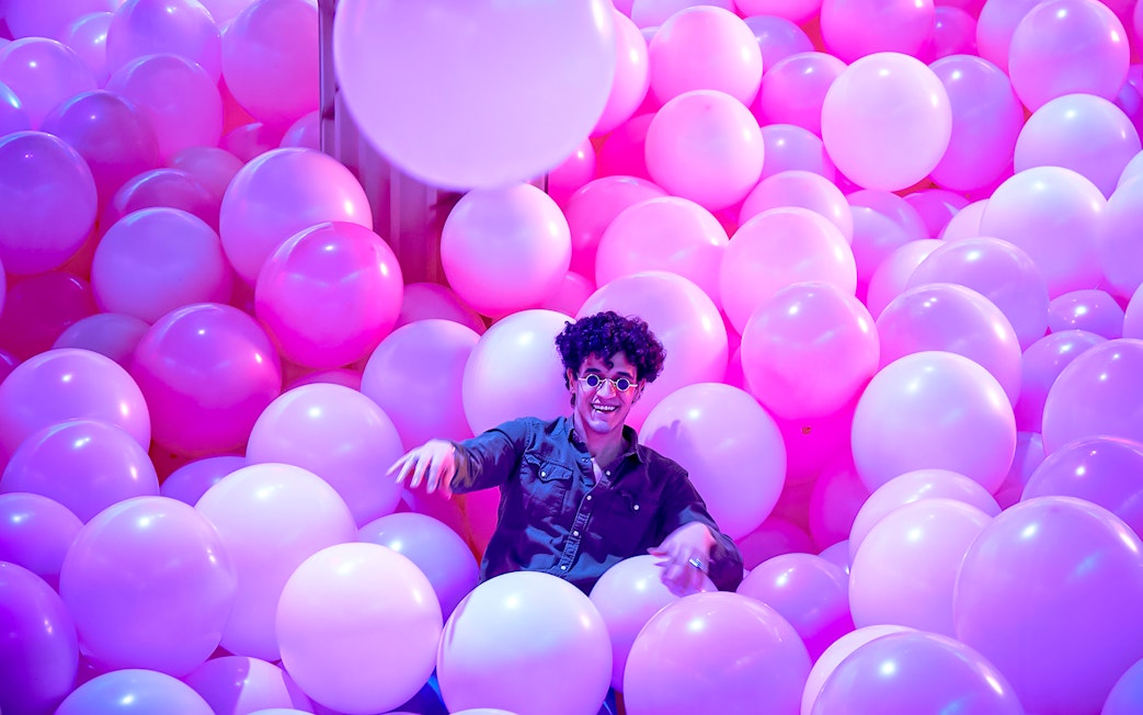 Person enjoying a room filled with pink and purple balloons at Bubble Planet, Washington DC.