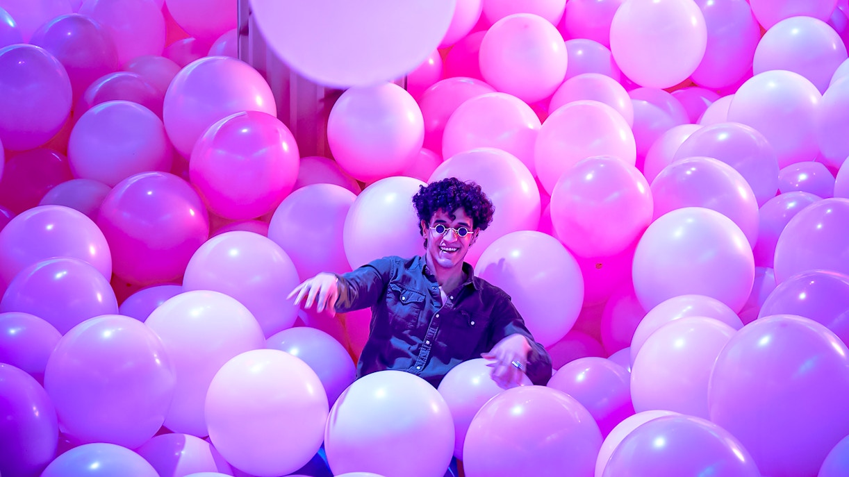 Person enjoying a room filled with pink and purple balloons at Bubble Planet, Washington DC.