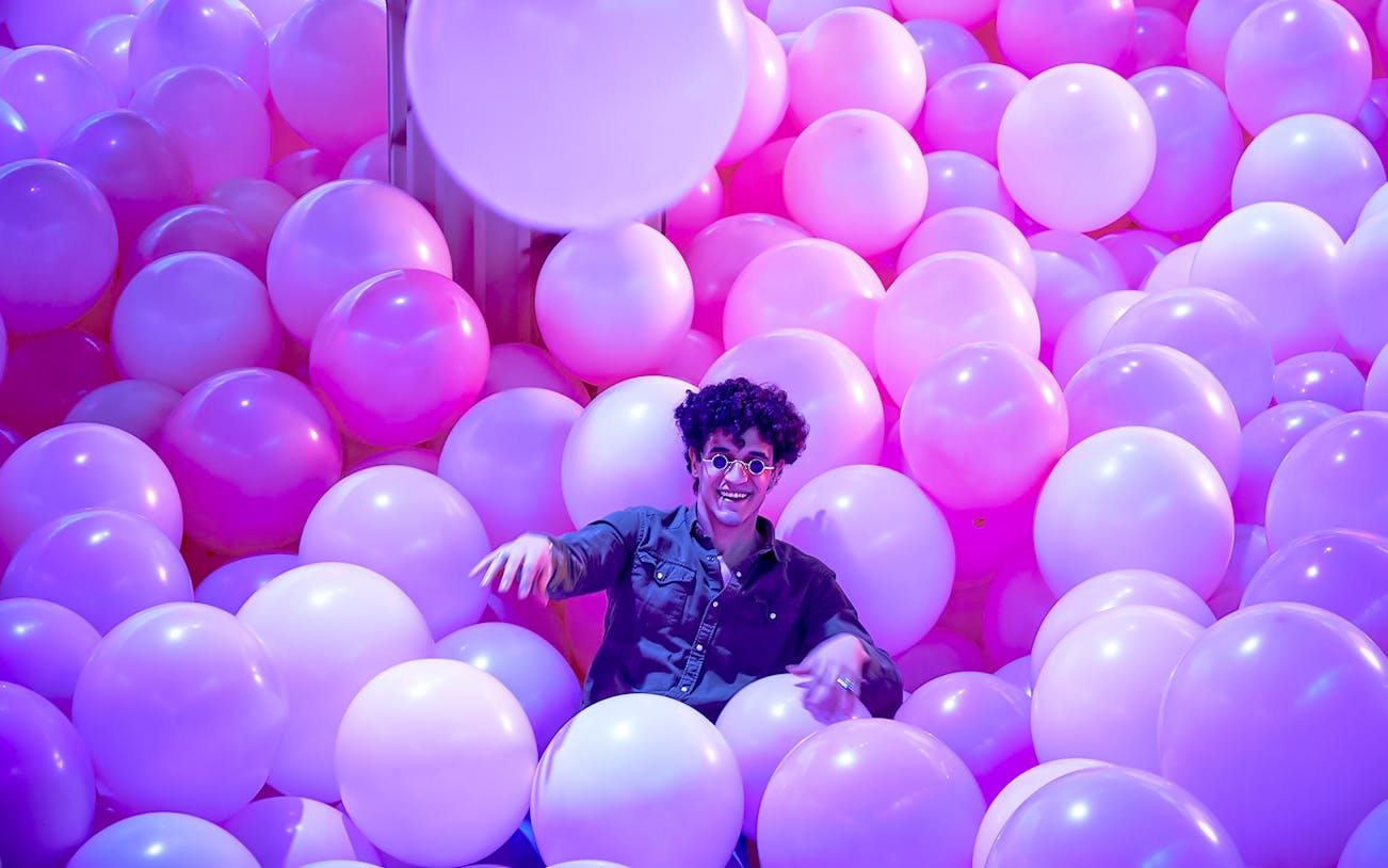 Person enjoying a room filled with pink and purple balloons at Bubble Planet, Washington DC.