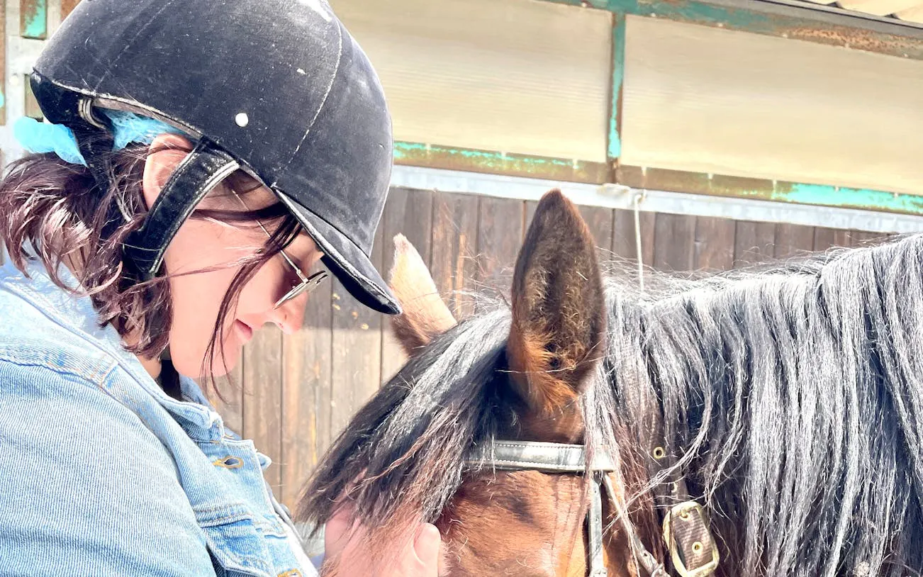 Horseback rider in helmet bonding with horse during Tuscany winery tour.