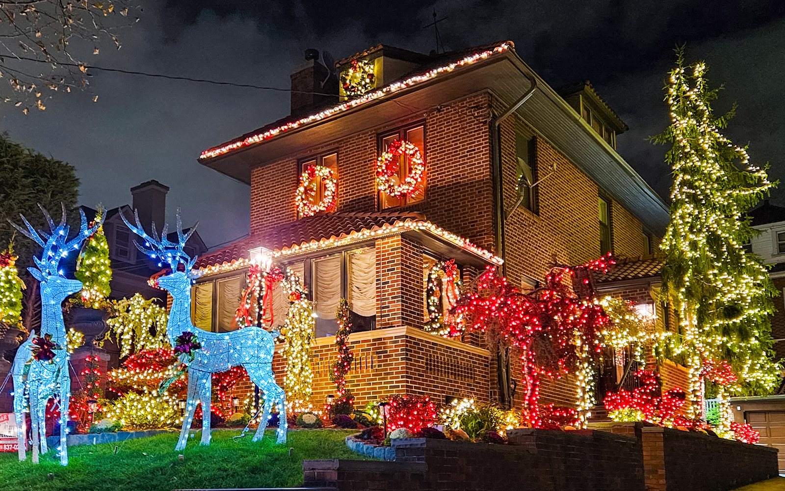 Brick house adorned with colorful Christmas lights and illuminated reindeer, New York bus tour.