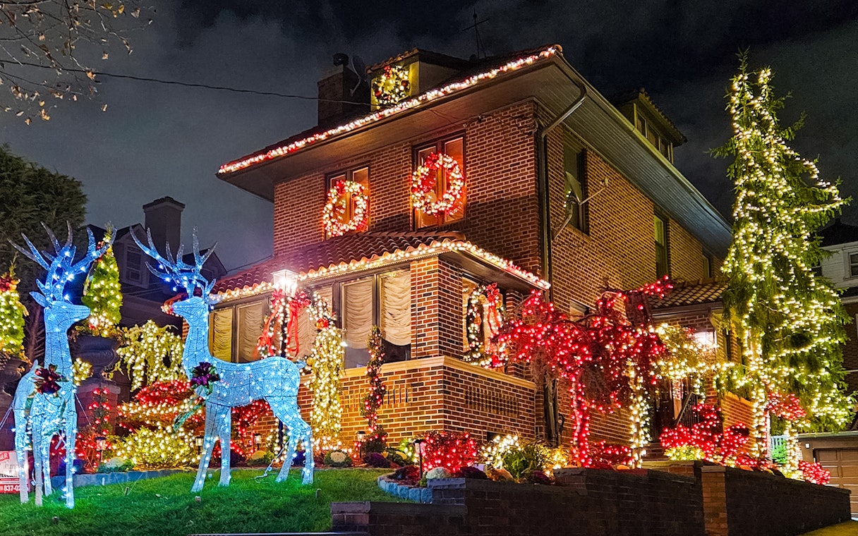 Brick house adorned with colorful Christmas lights and illuminated reindeer, New York bus tour.