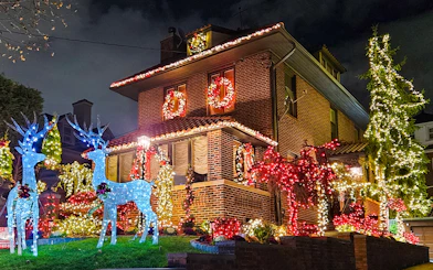 Brick house adorned with colorful Christmas lights and illuminated reindeer, New York bus tour.