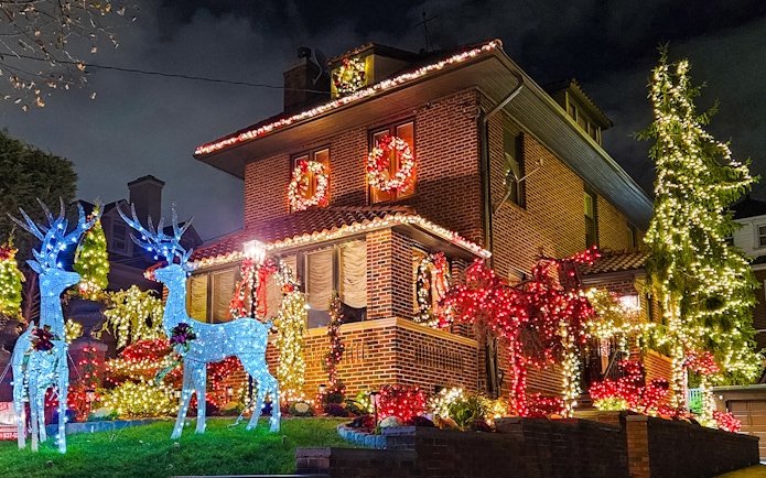 Brick house adorned with colorful Christmas lights and illuminated reindeer, New York bus tour.