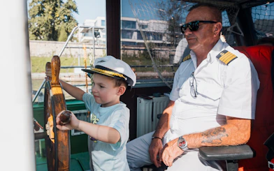 Child steering a boat with captain on a Krakow river sightseeing cruise.