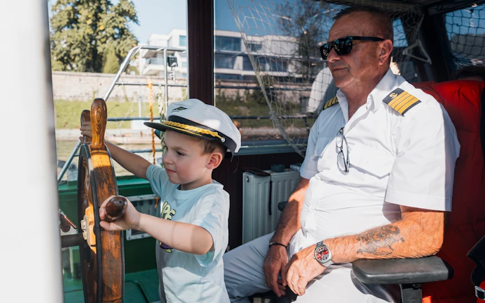 Child steering a boat with captain on a Krakow river sightseeing cruise.