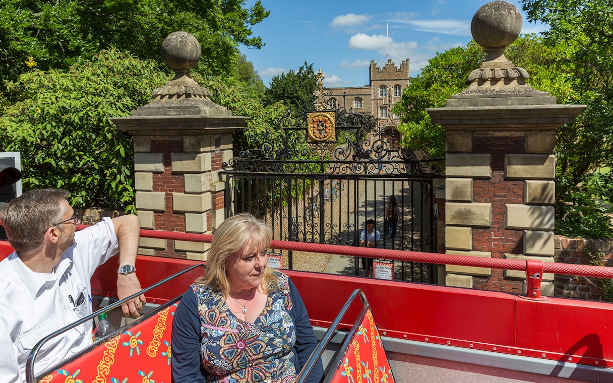 Open-top bus passing historic gate on Cambridge Hop-On Hop-Off Tour.