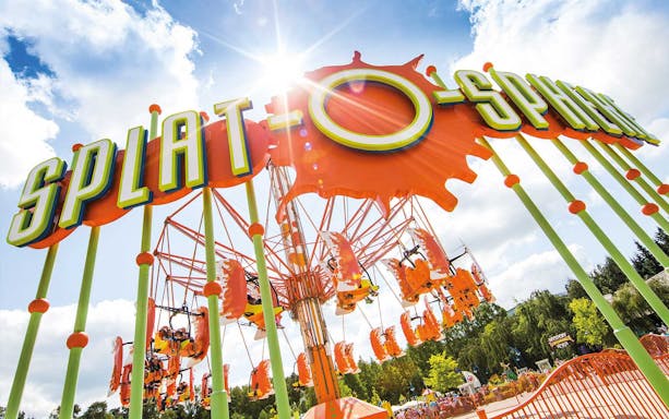 Splat-O-Sphere ride with orange swings and green poles under a sunny sky.
