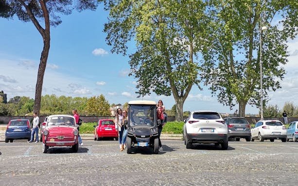 Guests in a golf cart at Orange Garden, Rome, with parked cars and trees in the background.