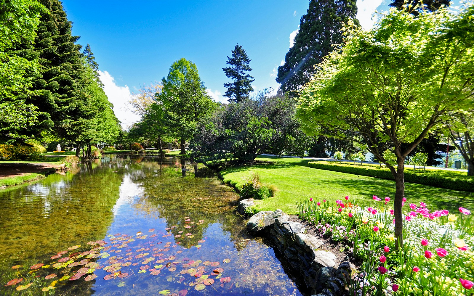 Queenstown Gardens New Zealand with lake, trees, and flower beds.