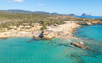 Cala Conta beach with clear turquoise water and sunbathers, Ibiza, Spain.