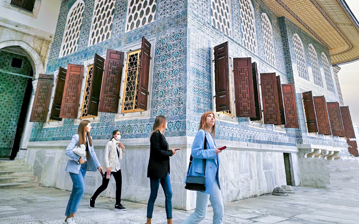 Visitors walking by the ornate tile walls of Topkapi Palace Harem in Istanbul.