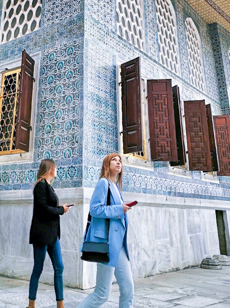 Visitors walking by the ornate tile walls of Topkapi Palace Harem in Istanbul.