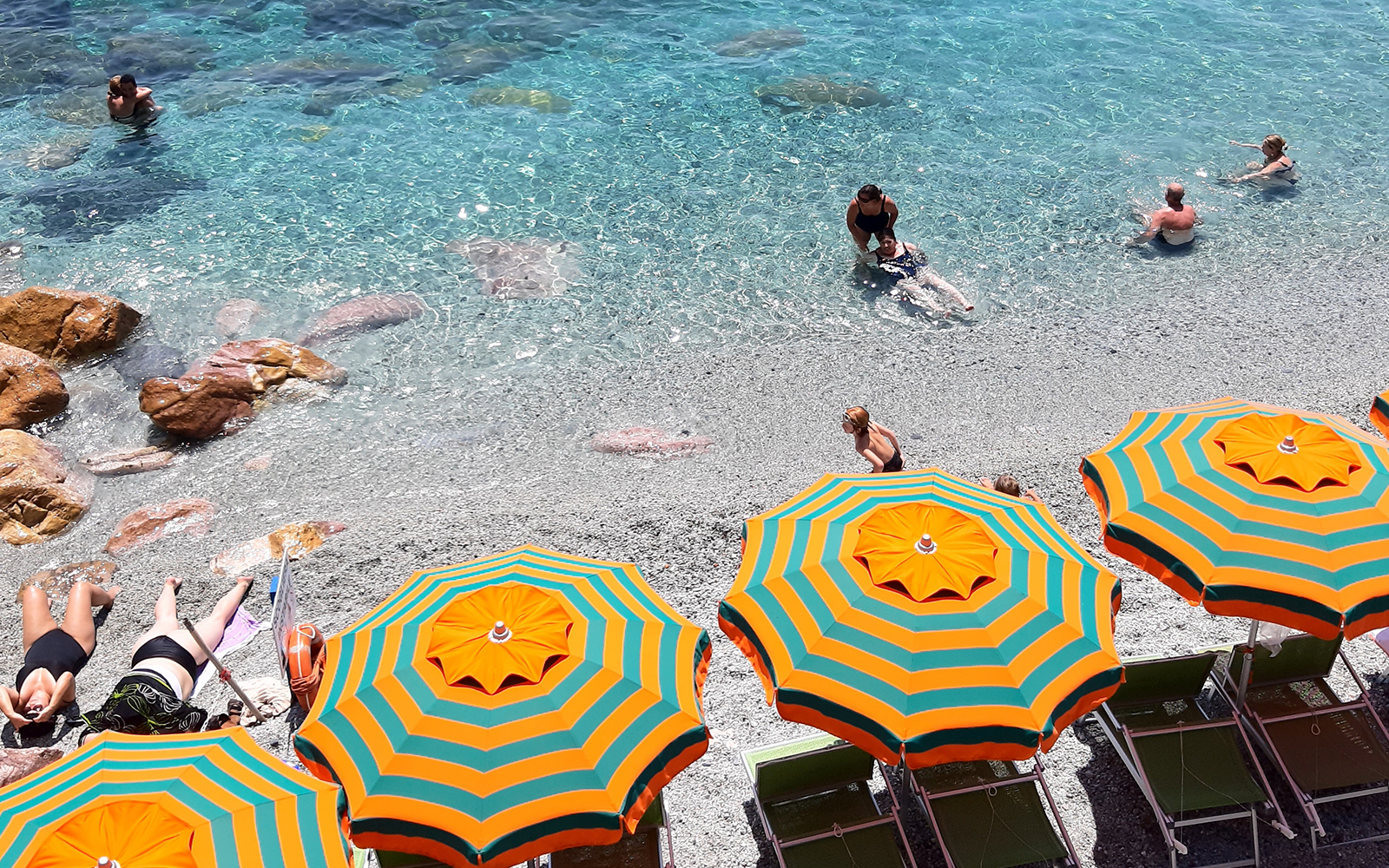 Beachgoers enjoying the clear waters and colorful umbrellas in Cinque Terre, Italy.