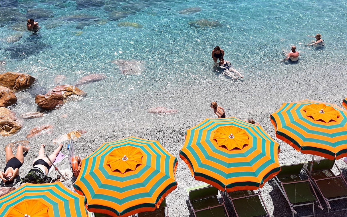 Beachgoers enjoying the clear waters and colorful umbrellas in Cinque Terre, Italy.