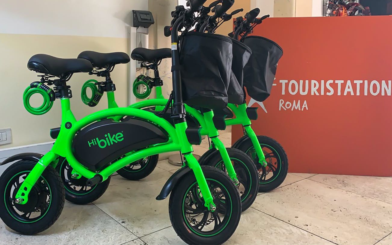 Green e-bikes lined up at a rental station in Rome.