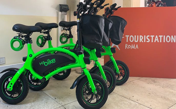 Green e-bikes lined up at a rental station in Rome.