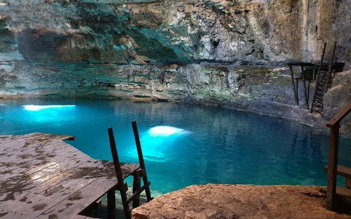 Underground cenote with clear blue water and rocky walls, part of World Wonder Discovery Guided Tour.