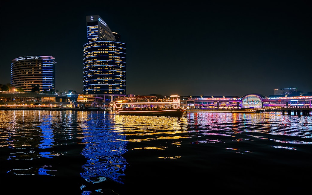 Dubai Canal at night with illuminated cruise boat and city skyline.