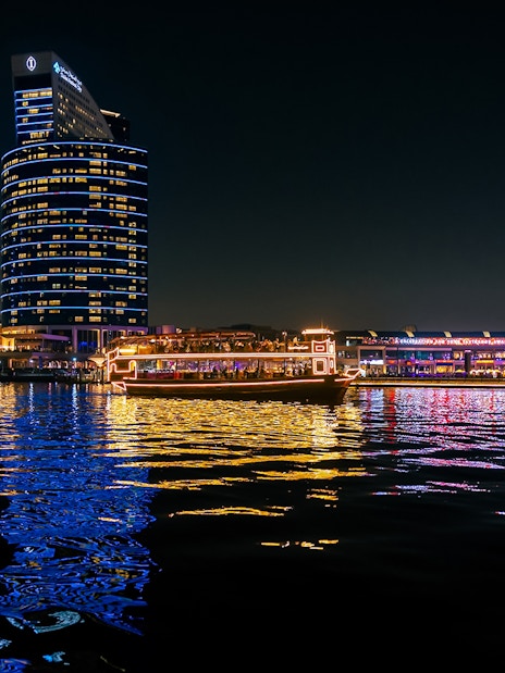 Dubai Canal at night with illuminated cruise boat and city skyline.