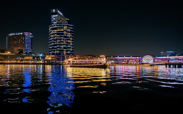 Dubai Canal at night with illuminated cruise boat and city skyline.