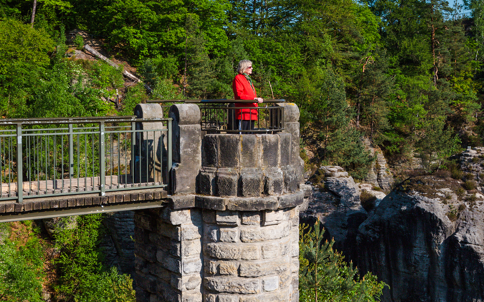 Woman standing at viewpoint on Bastion Bridge, surrounded by lush greenery and rocky cliffs.