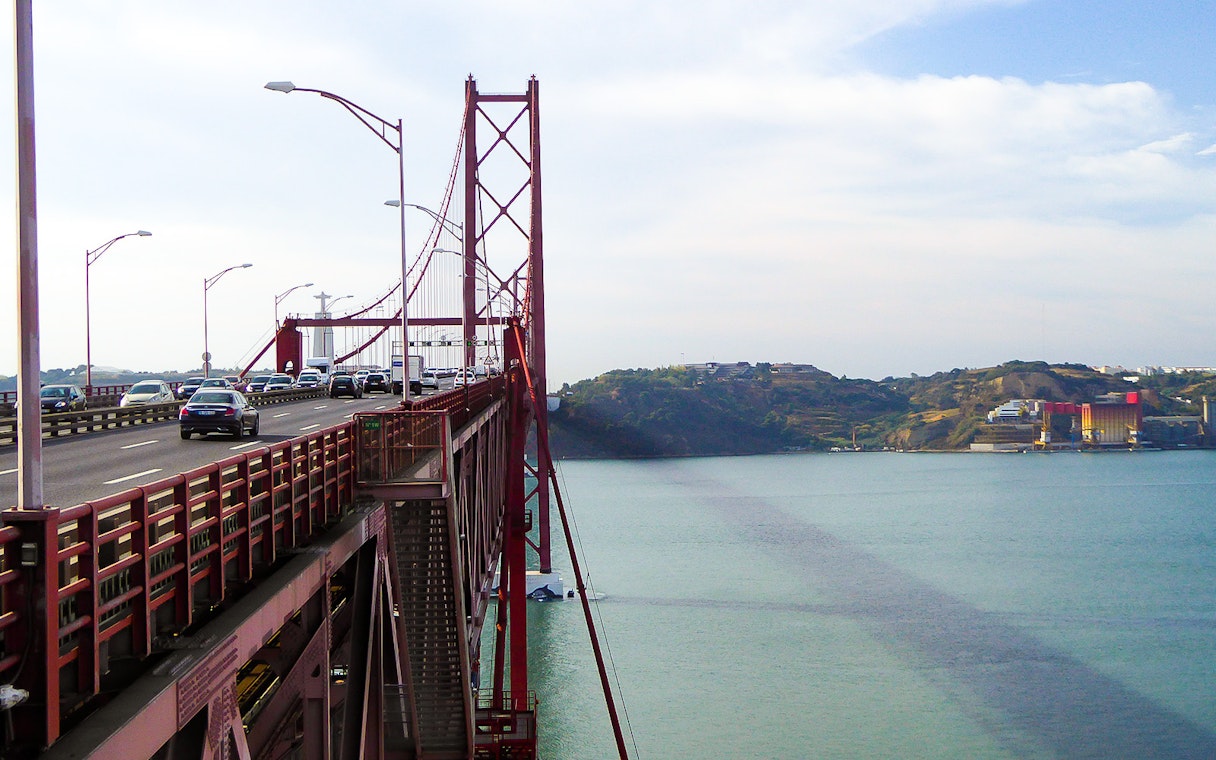 Cars crossing the 25 de Abril Bridge in Lisbon with Cristo Rei statue in the background.
