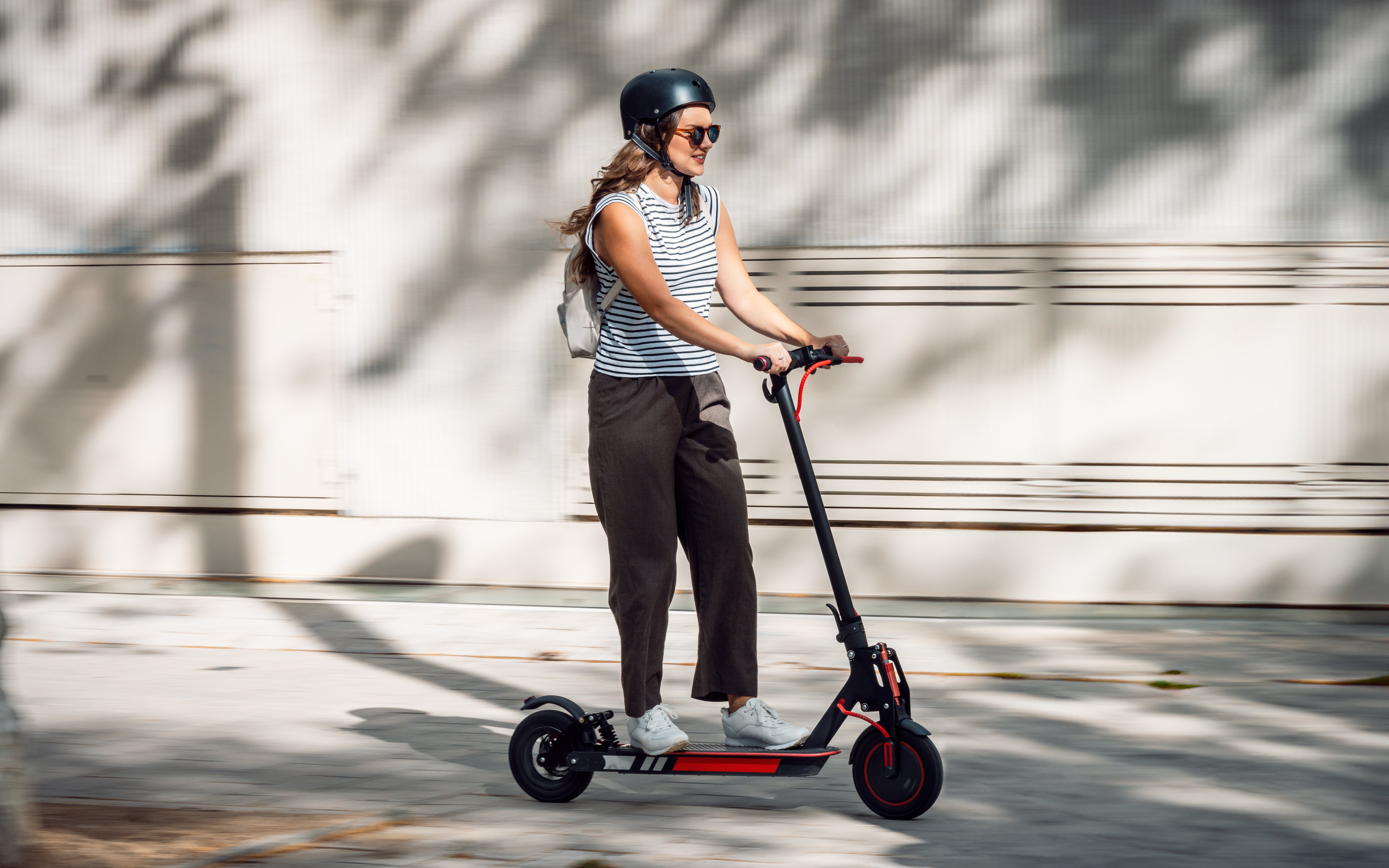 Woman riding an e-scooter on a sunny urban street.