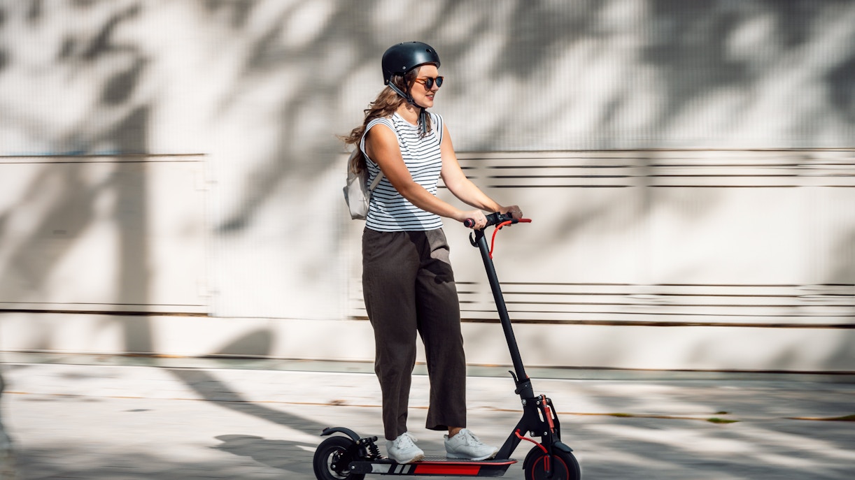 Woman riding an e-scooter on a sunny urban street.